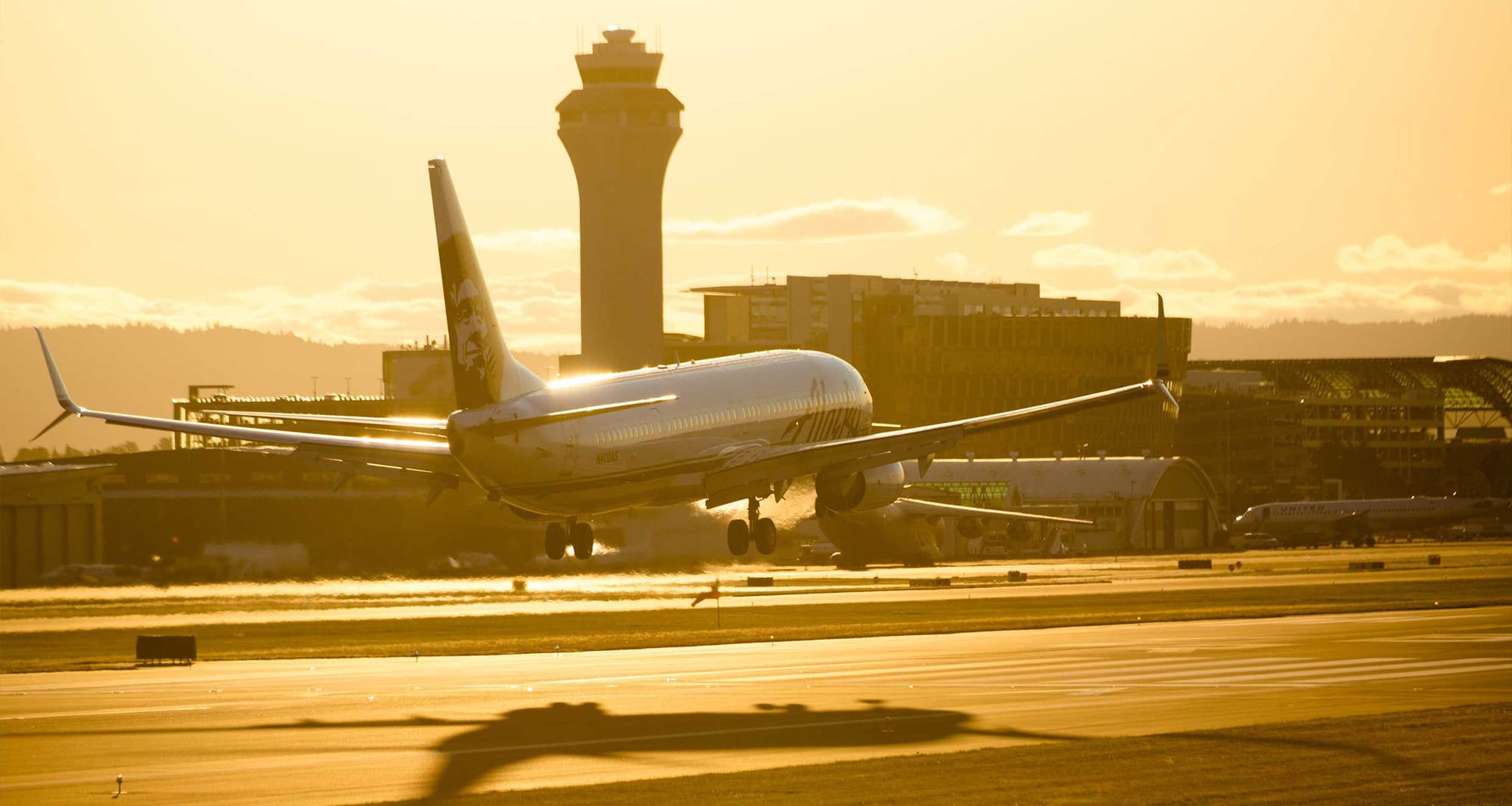 Alaska Airlines plane landing at sunset.