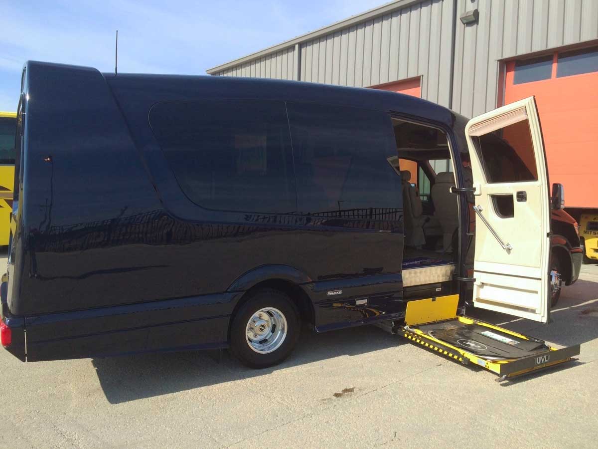 Wheelchair lift deployed from underneath black Mercedes Sprinter van.