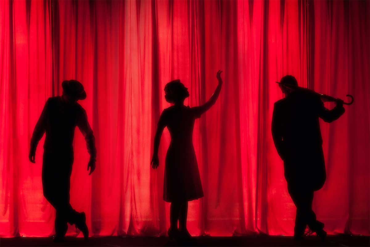 Silhouettes of three actors onstage in front of a red curtain.