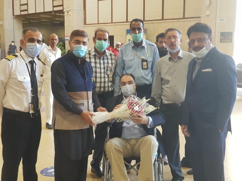 Man on wheelchair holding flowers, surrounded by airline executives at airport.