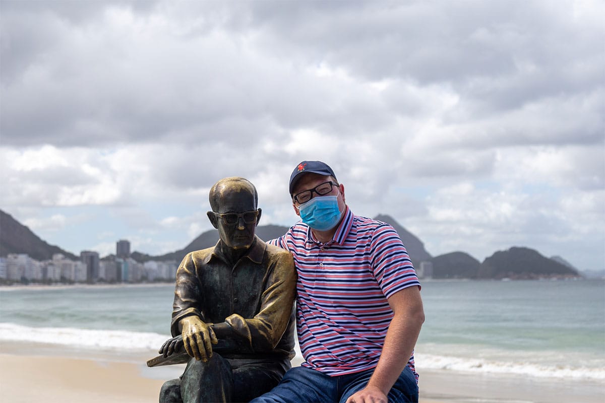 John sitting on a bench with his arm around a statue.