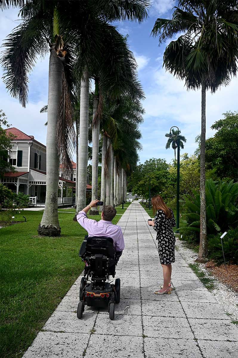 John rolling down sidewalk lined with palm trees towards the Edison estate.