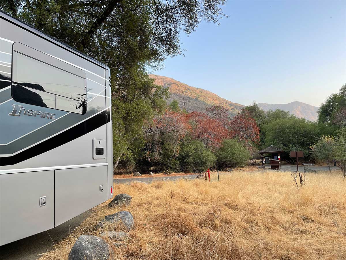 Rear quarter of Winnebago Inspire RV in front of a picturesque field and mountain in the background.