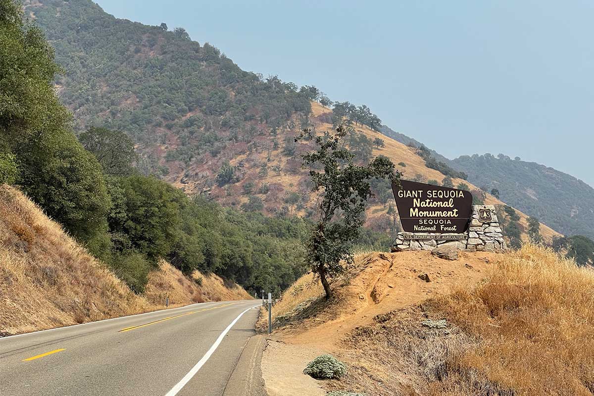 Giant Sequoia National Monument sign along road through hilly terrain.