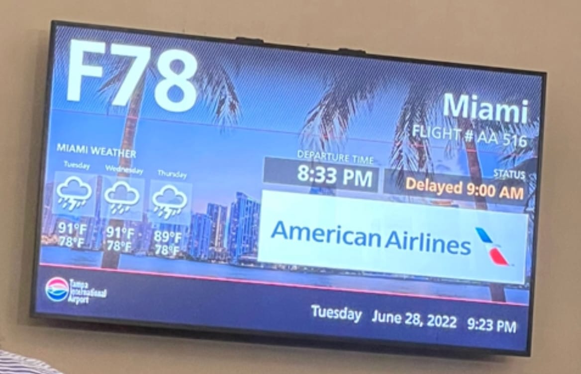 Gate monitor showing American Airlines flight delayed more than 12 hours to a 9 a.m. departure time.