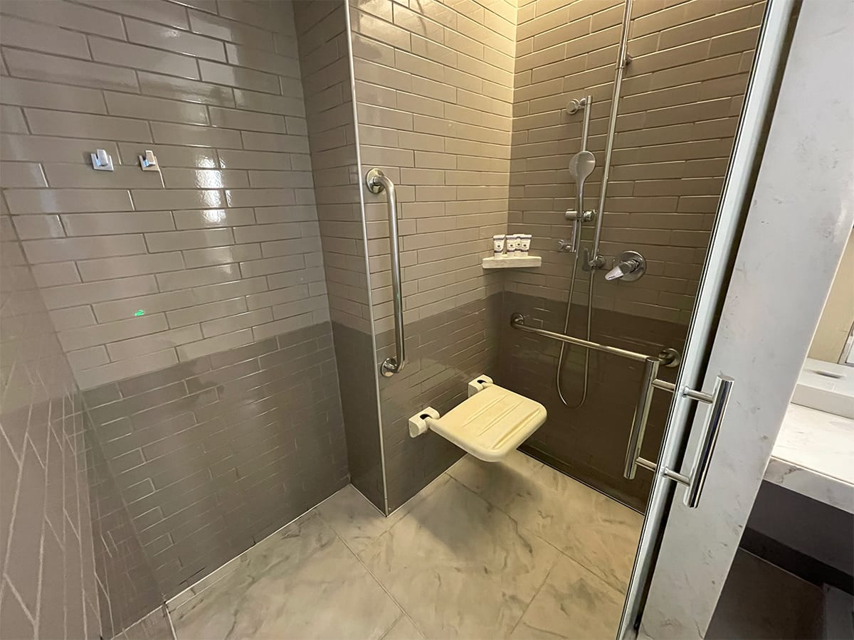 Roll-in shower with wall-mounted seat, handheld shower head and grab bars.