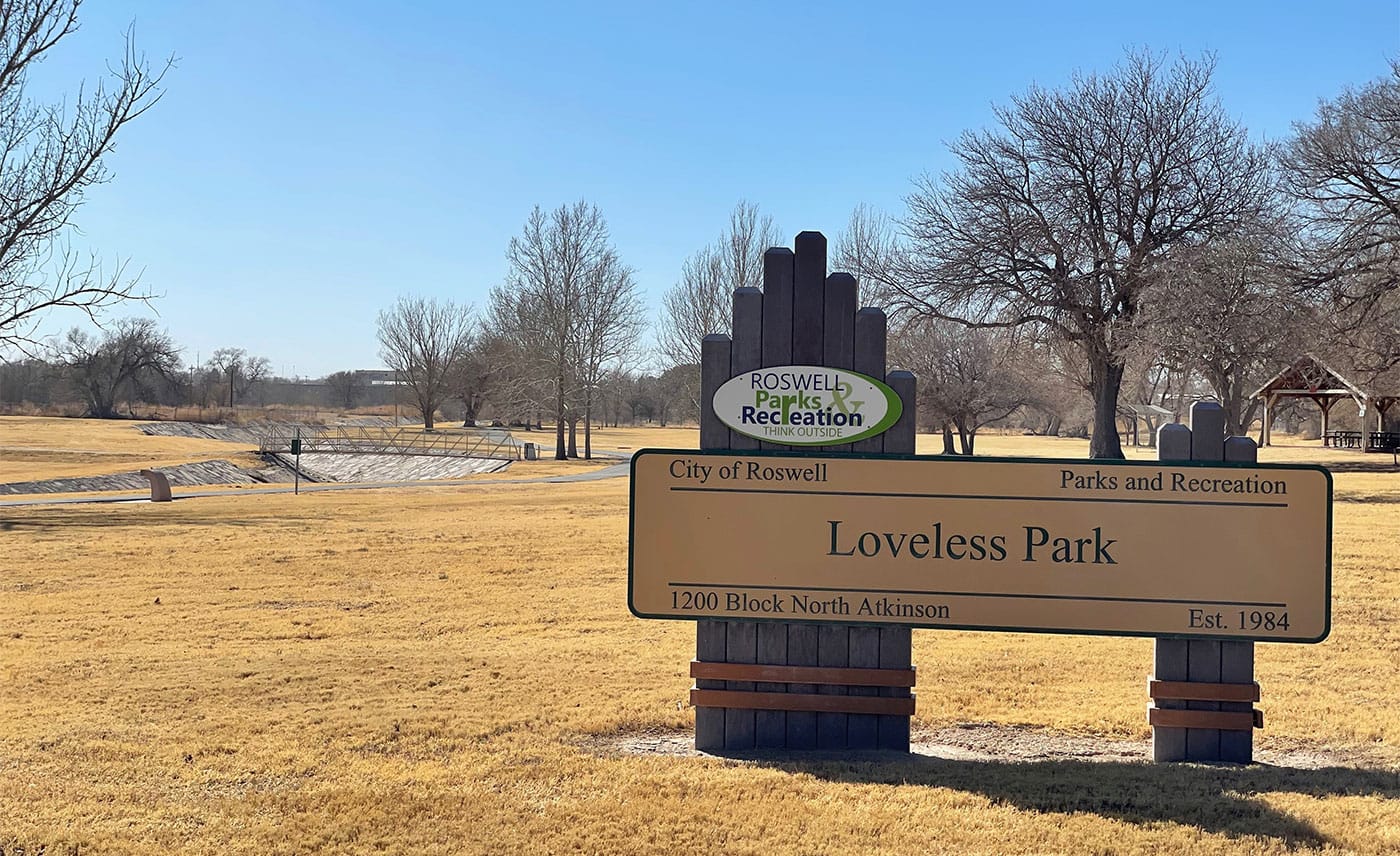 Loveless Park sign in front of an open field with trees and a paved pathway.