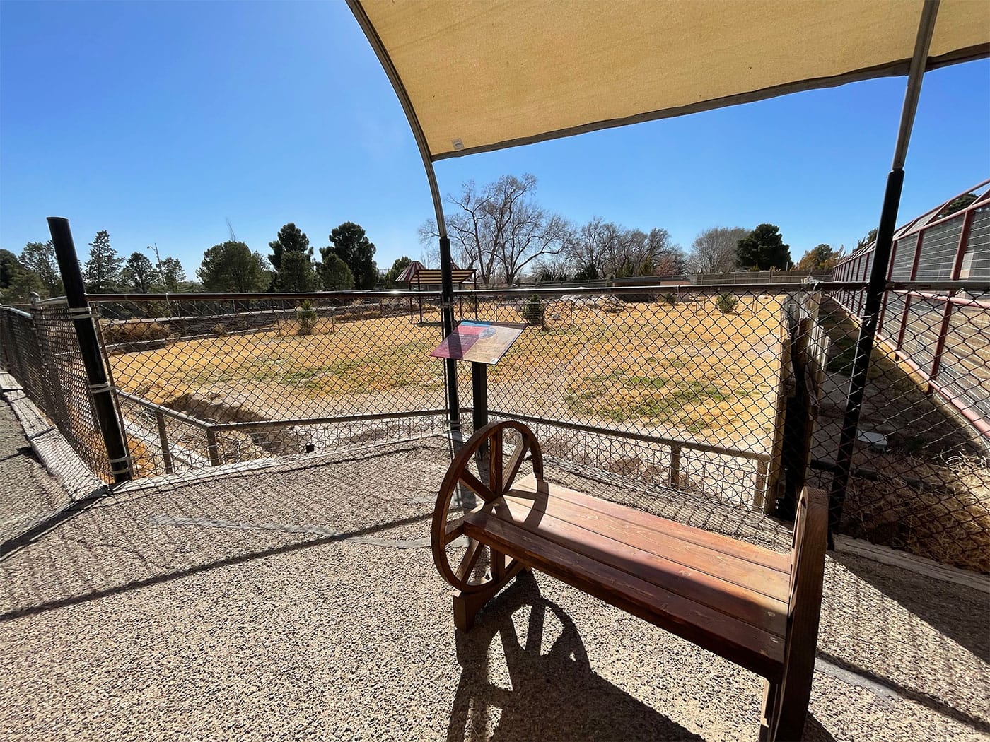 Bench under a shaded awning next to a zoo exhibit.