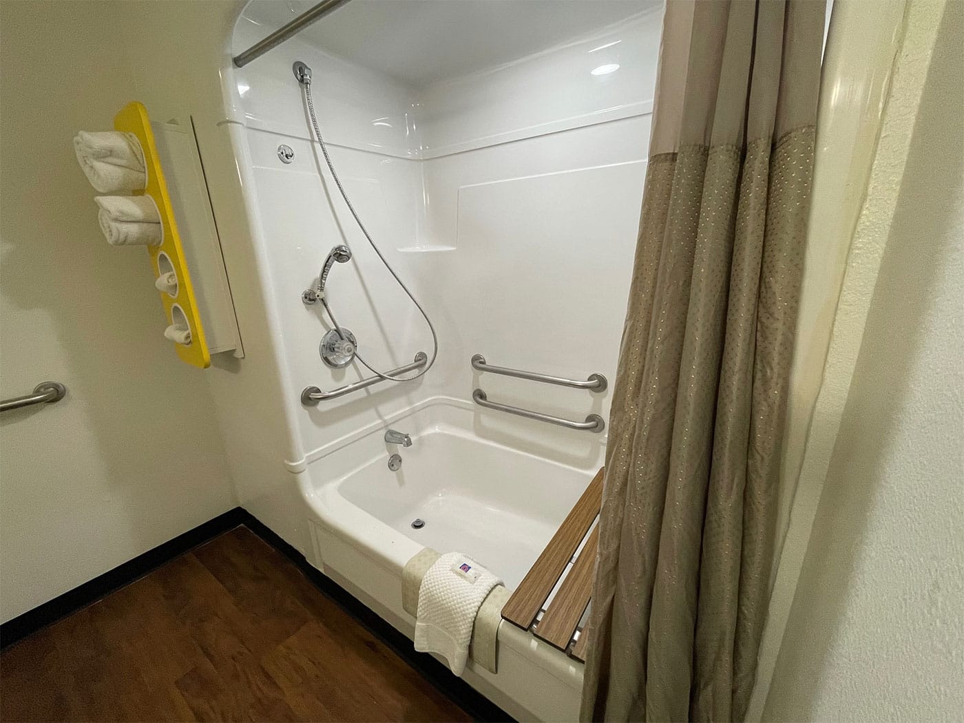 Bathtub with built-in seat, grab bars and handheld shower head.