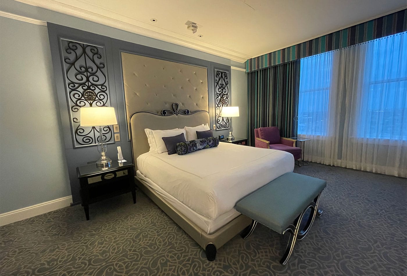 King size bed in luxury hotel room, with two large windows.