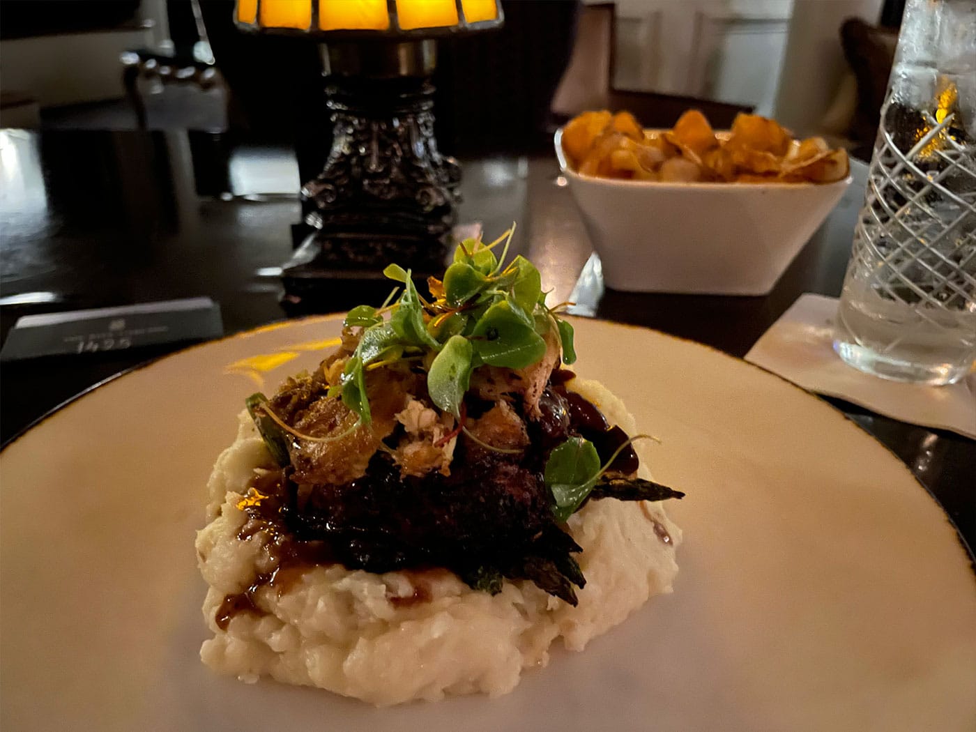 Filet mignon plated on a dining table with lamp.