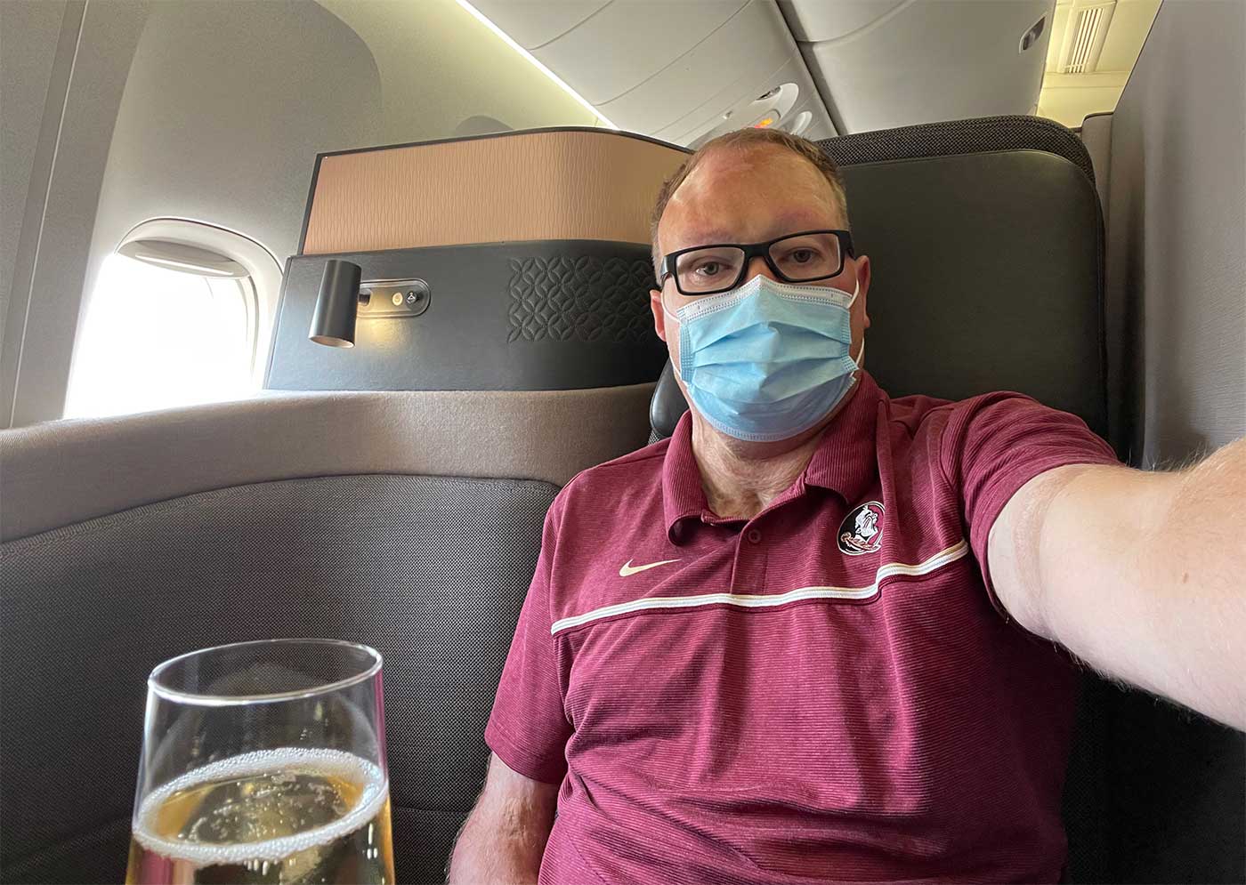 John taking a selfie while seated in the QSuite, with a glass of champagne pictured in the foreground.