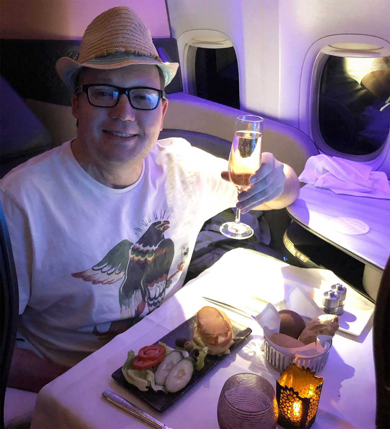 John wearing a bowler hat and while raising a glass of champagne in the Qatar Airways suite.