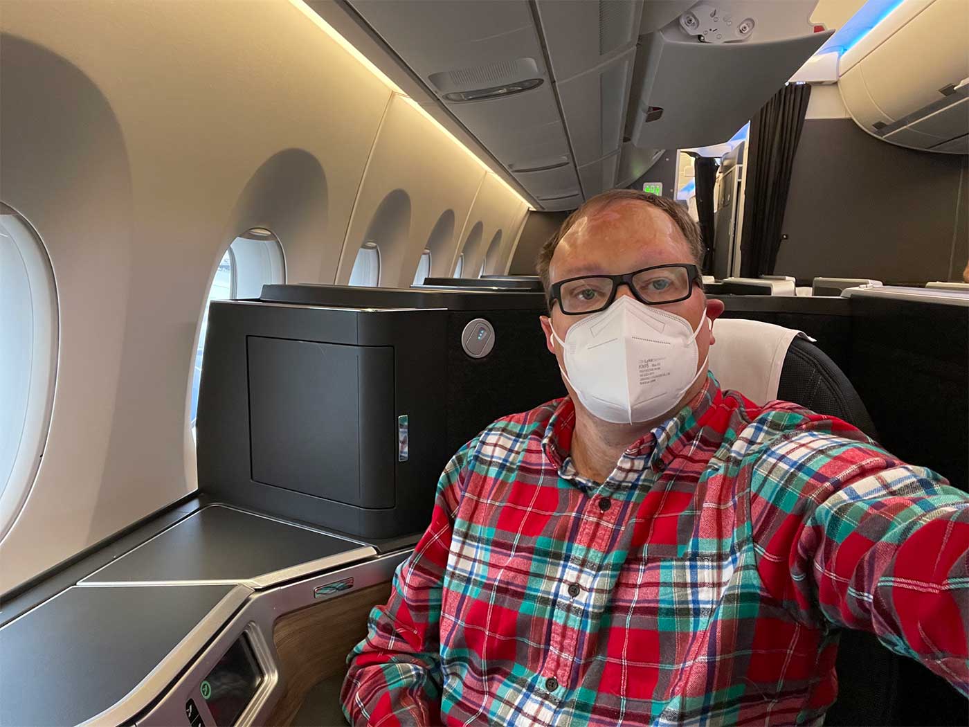 John wearing a flannel shirt while seated in the business class seat.