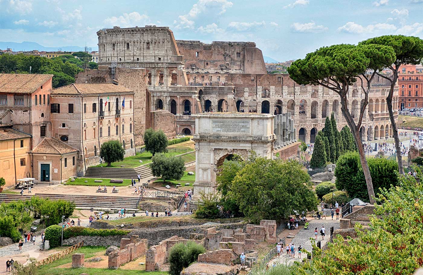 Colosseum seen from a hilltop with other ancient Roman ruins and artifacts in the foreground.