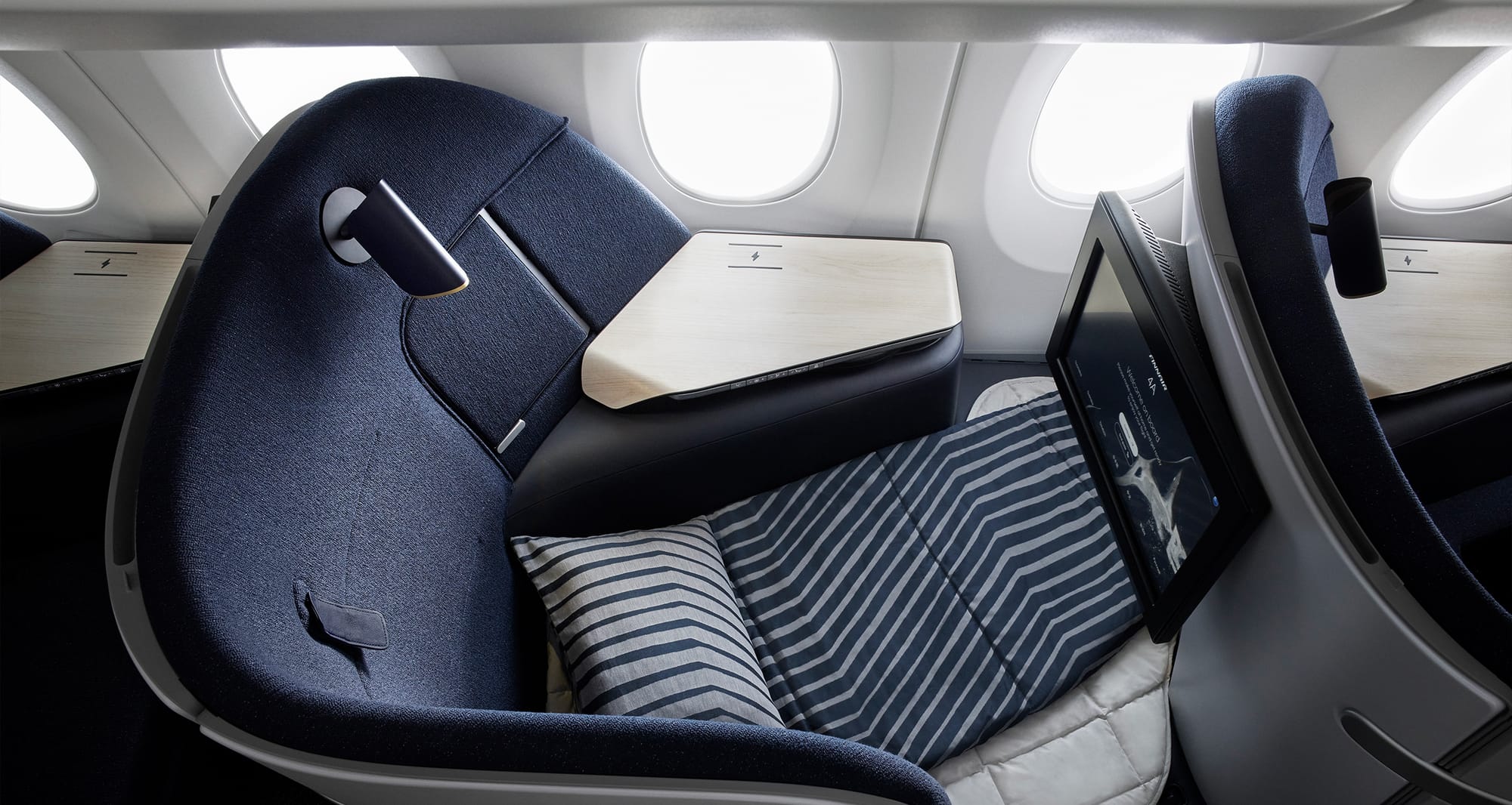 Finnair business class seat in lay flat bed mode with pillow and blanket.