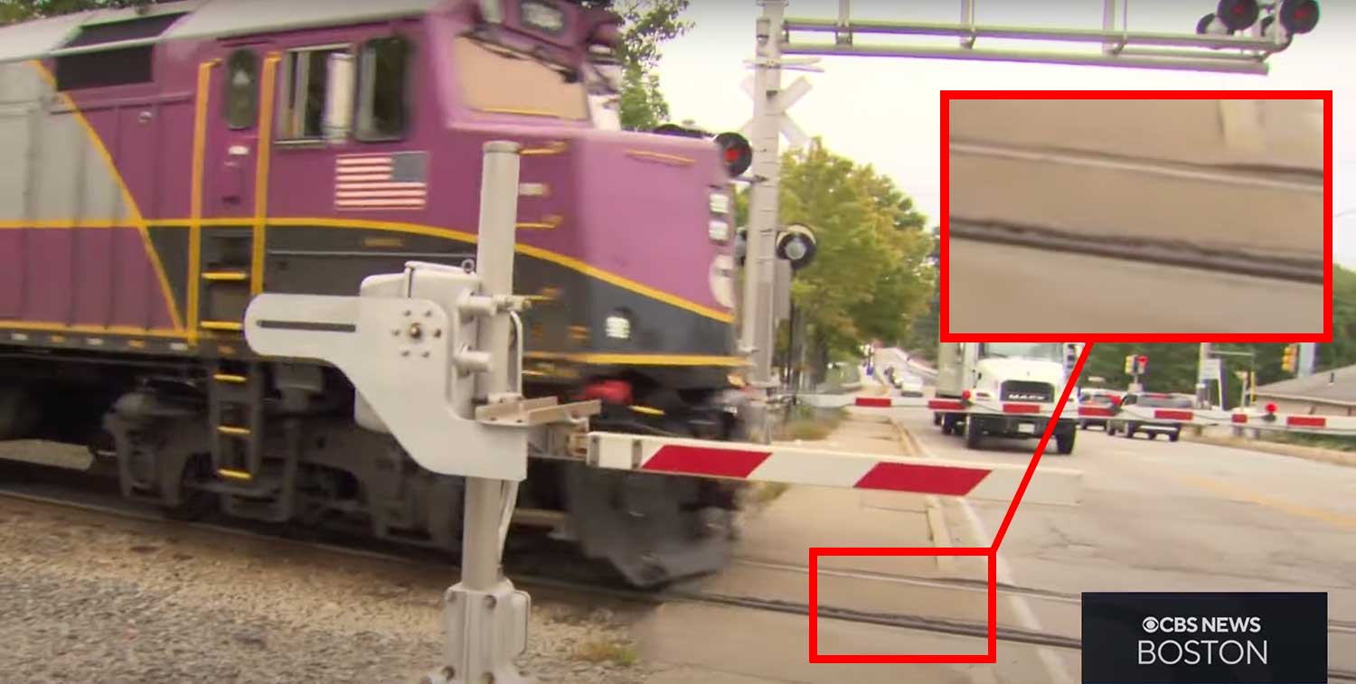 Zoomed view of uneven pavement around railroad tracks at crossing site.