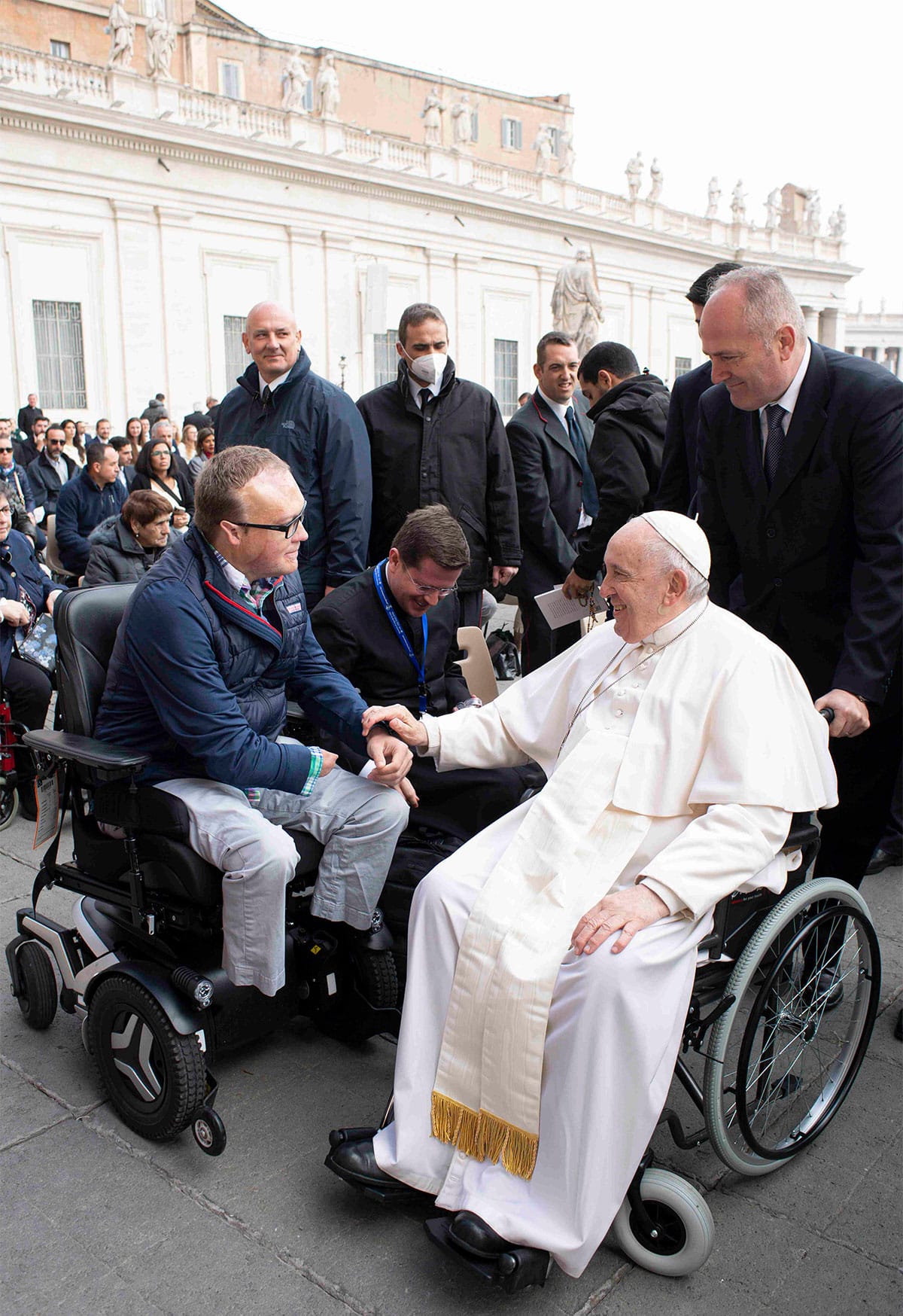 Pope Francis resting his hand on John's wrist as they greet each other in Saint Peter's Square.