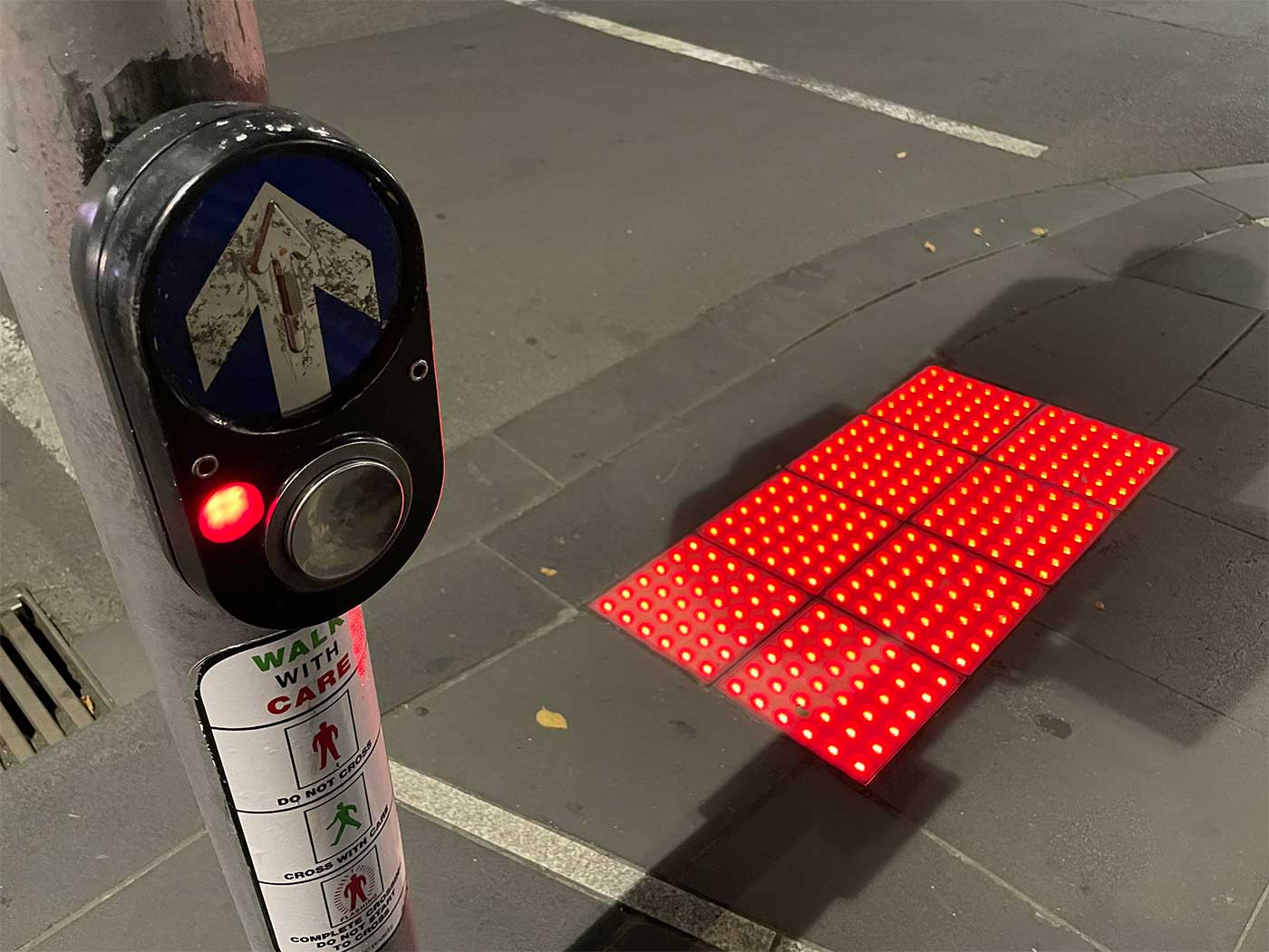 Red LED lights illuminated inside truncated domes at crosswalk intersection.