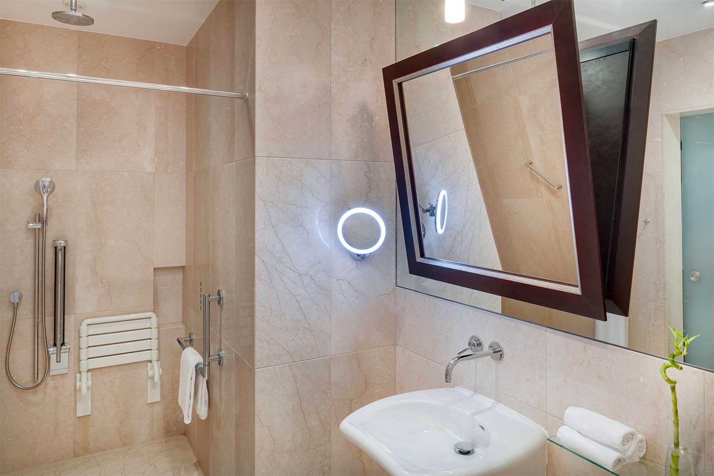 Accessible hotel bathroom with roll-in shower, shower seat and roll under sink.