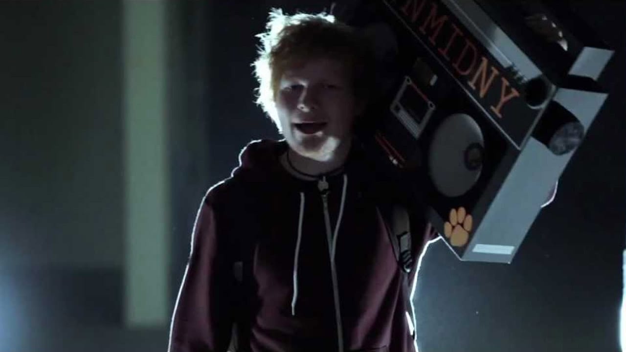 Ed Sheeran holding a large boom box over his shoulder.