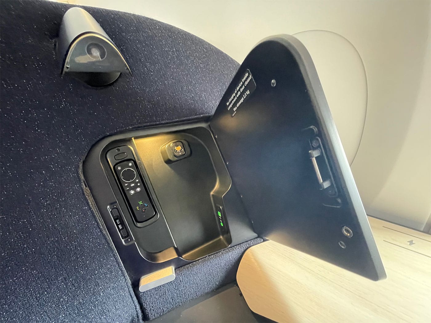 Door open on storage cabinet in seat back, with a remote and power outlets.