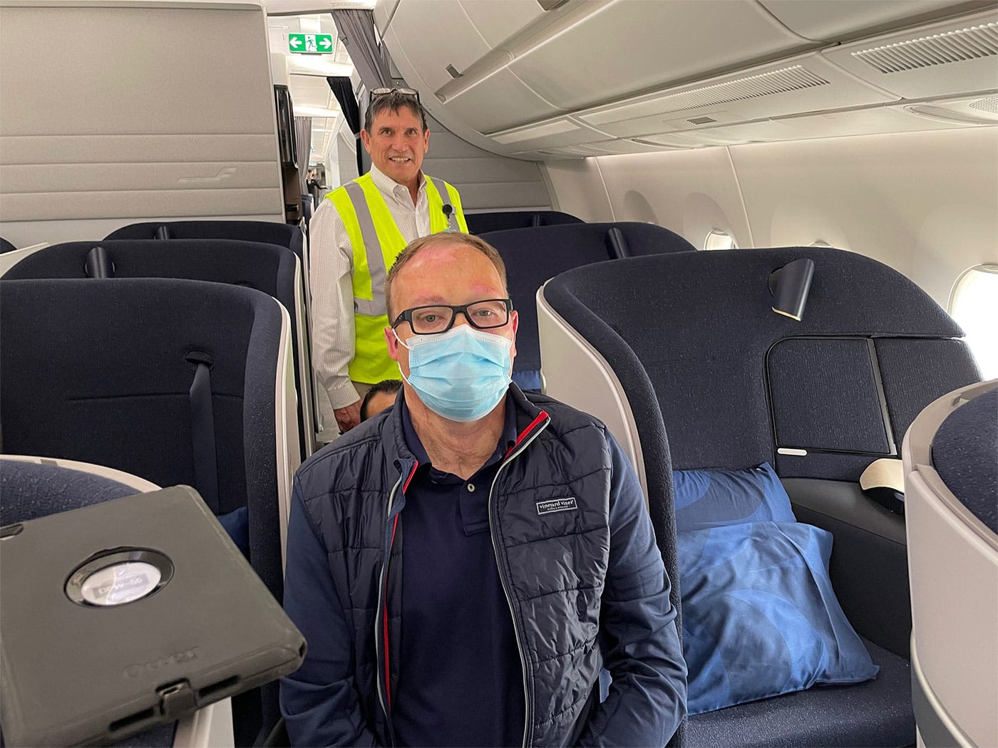 John seated in an aisle chair, next to his business class seat during boarding.