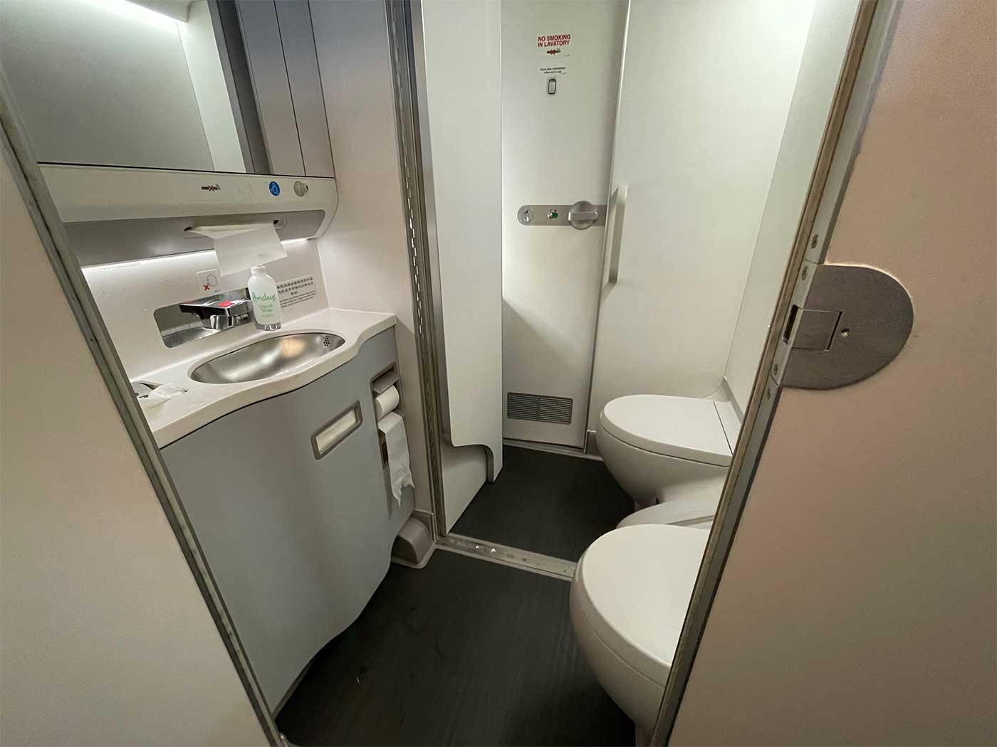 Airplane lavatory with opened dividing wall to reveal space of second standard lavatory.