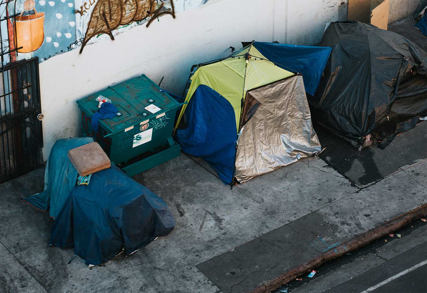 Tents used by homeless people set up on a sidewalk next to a building.