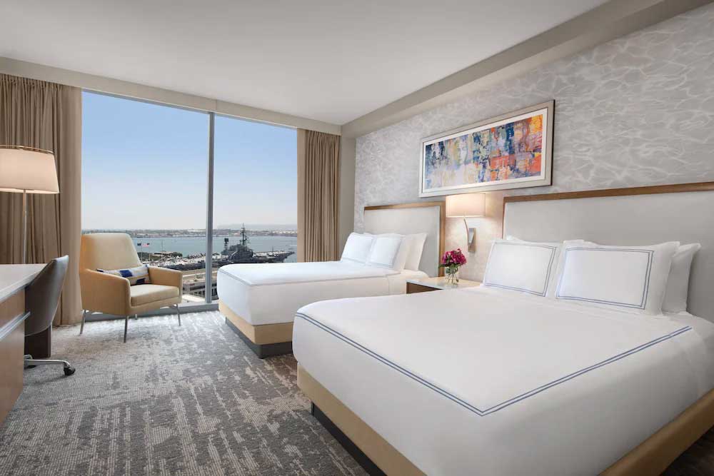 Hotel room with two beds looking out over the water with a battleship in the harbor.