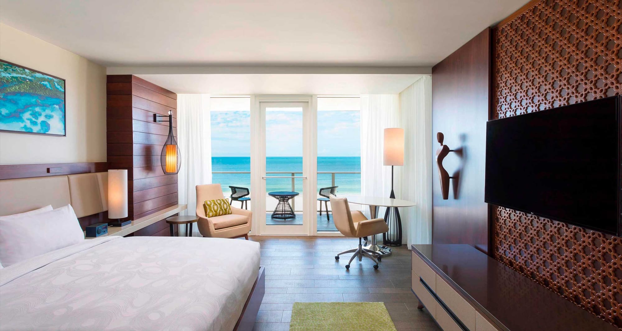 Hotel room with king size bed, wood floors and windows that look out over an oceanfront balcony.