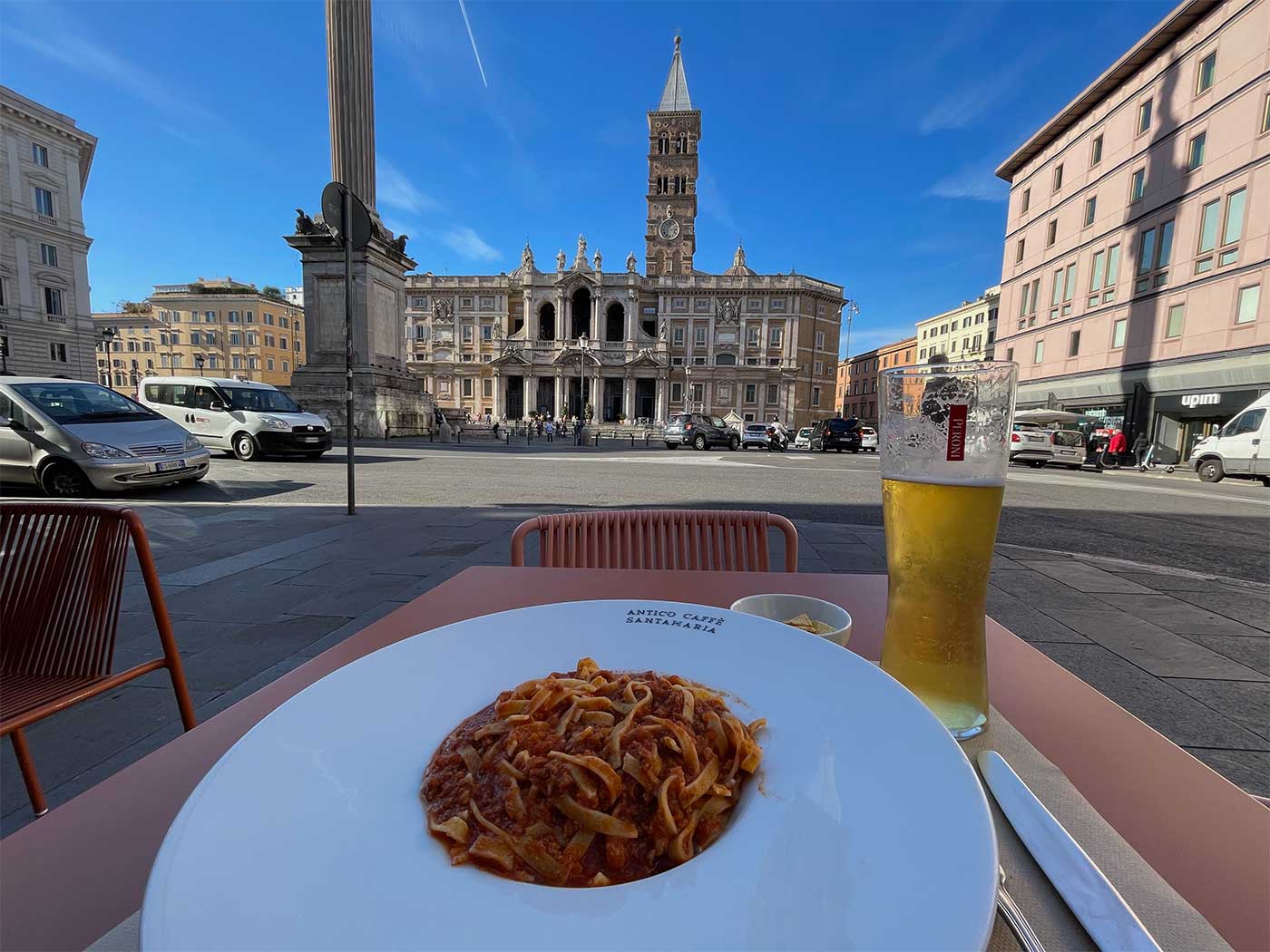 Pasta dish on an outdoor restaurant table with a large church in the distance.