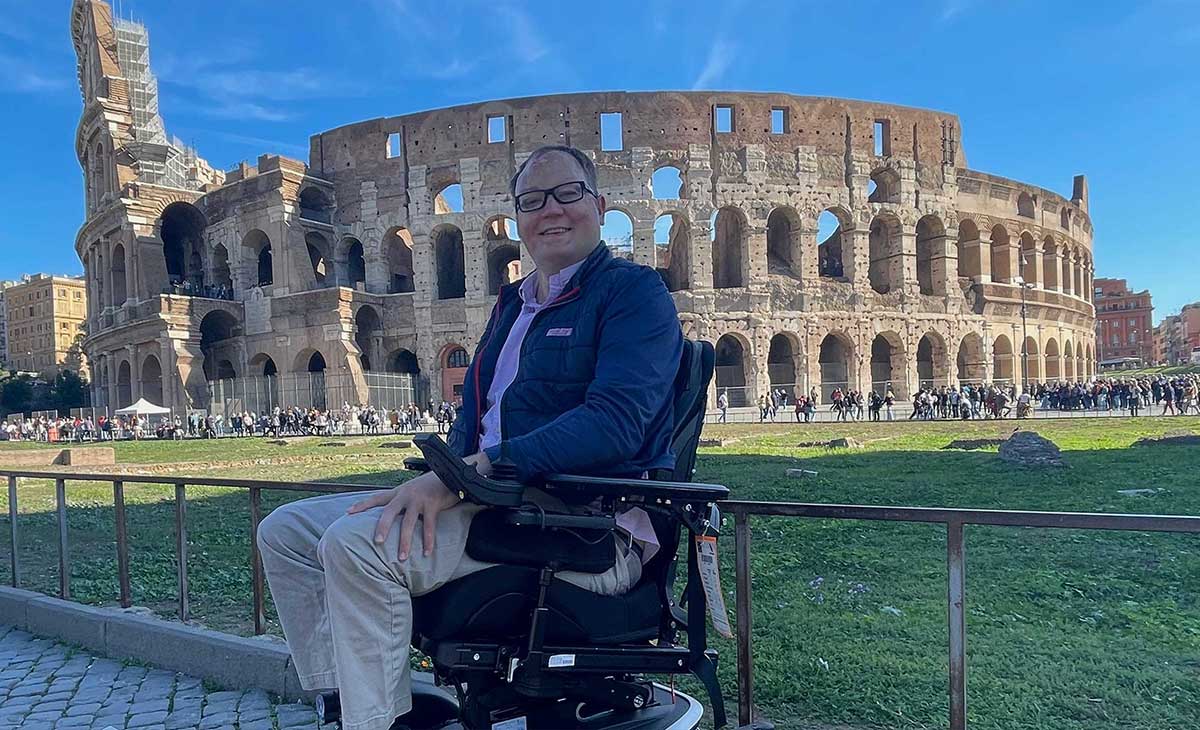 John seated in his wheelchair in front of the Colosseum in Rome, Italy.