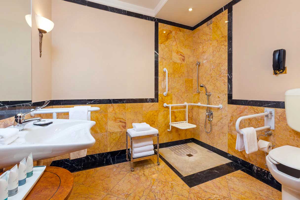 Accessible bathroom with roll-in shower, shower chair, sink and toilet with grab bars.