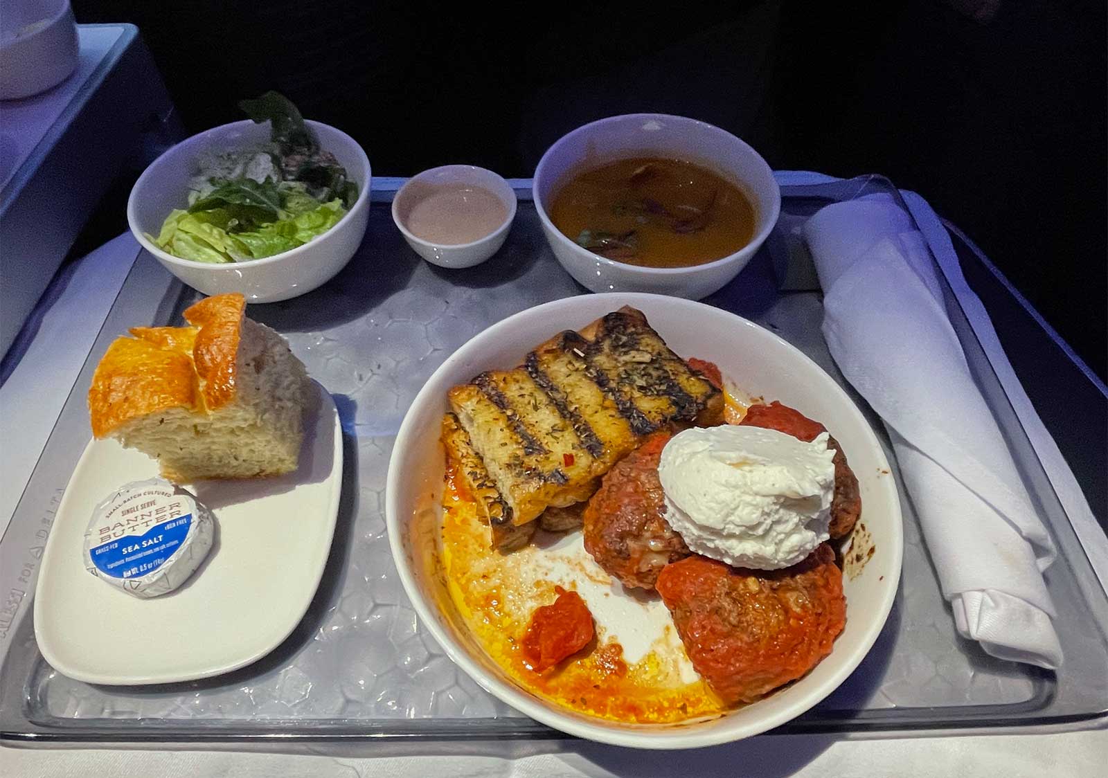 Meal of meatballs, salad, soup and more on a tray table.