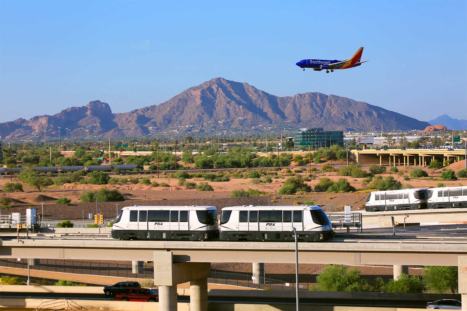 Southwest airplane landing behind two trains crossing a bridge.