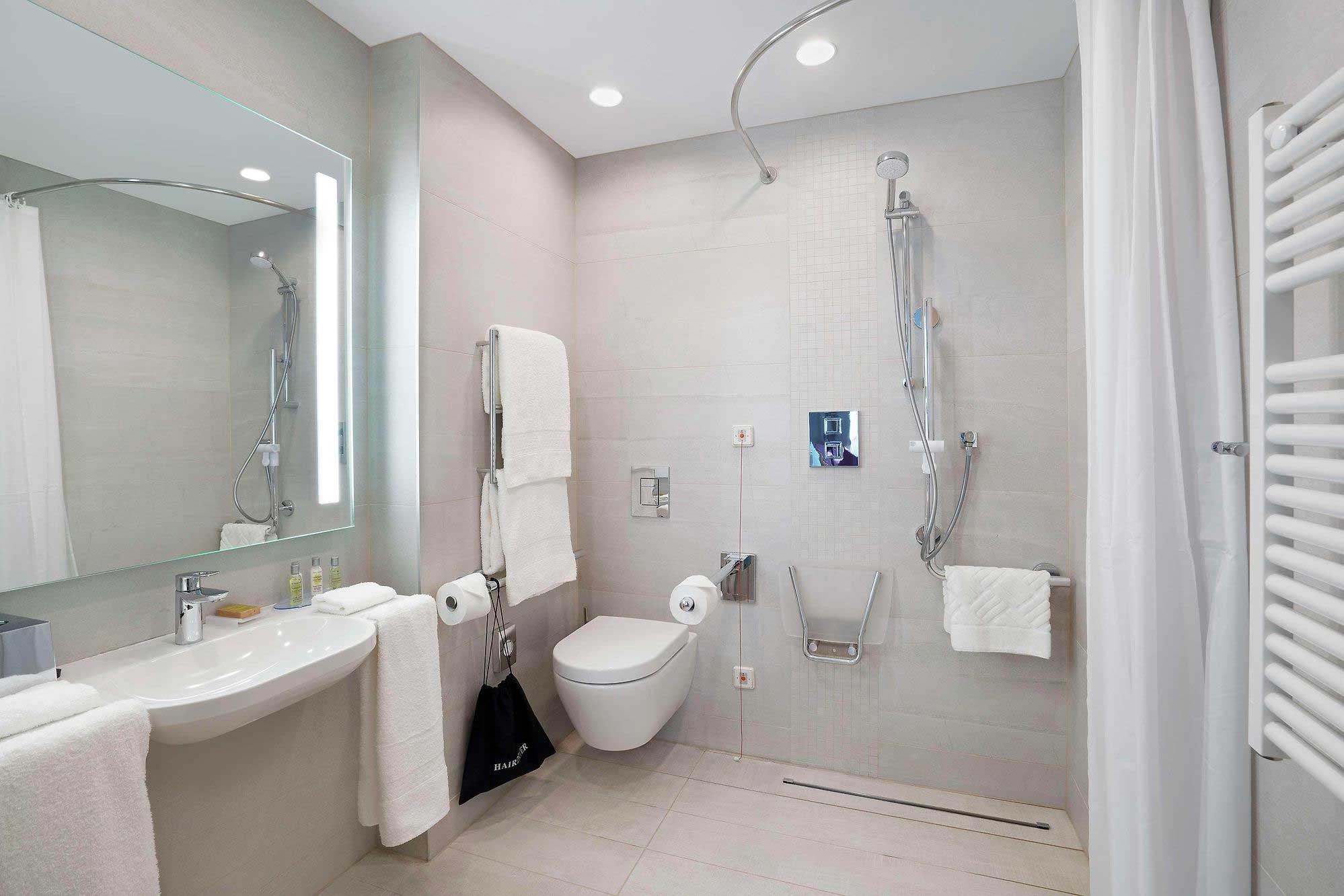 Accessible hotel bathroom with roll-in shower, shower seat and roll under sink.