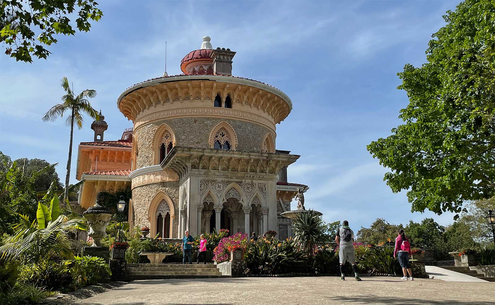 Circular palace facade surrounded by lush greenery, trees and flowers.