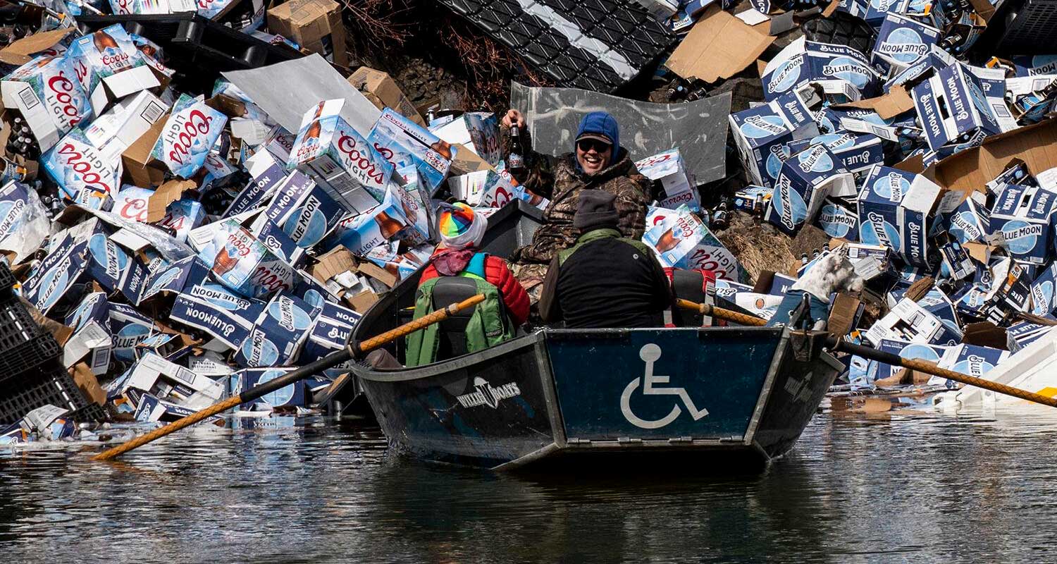 Peopler in wheelchair accessible boat collecting beer cans from derailed train.