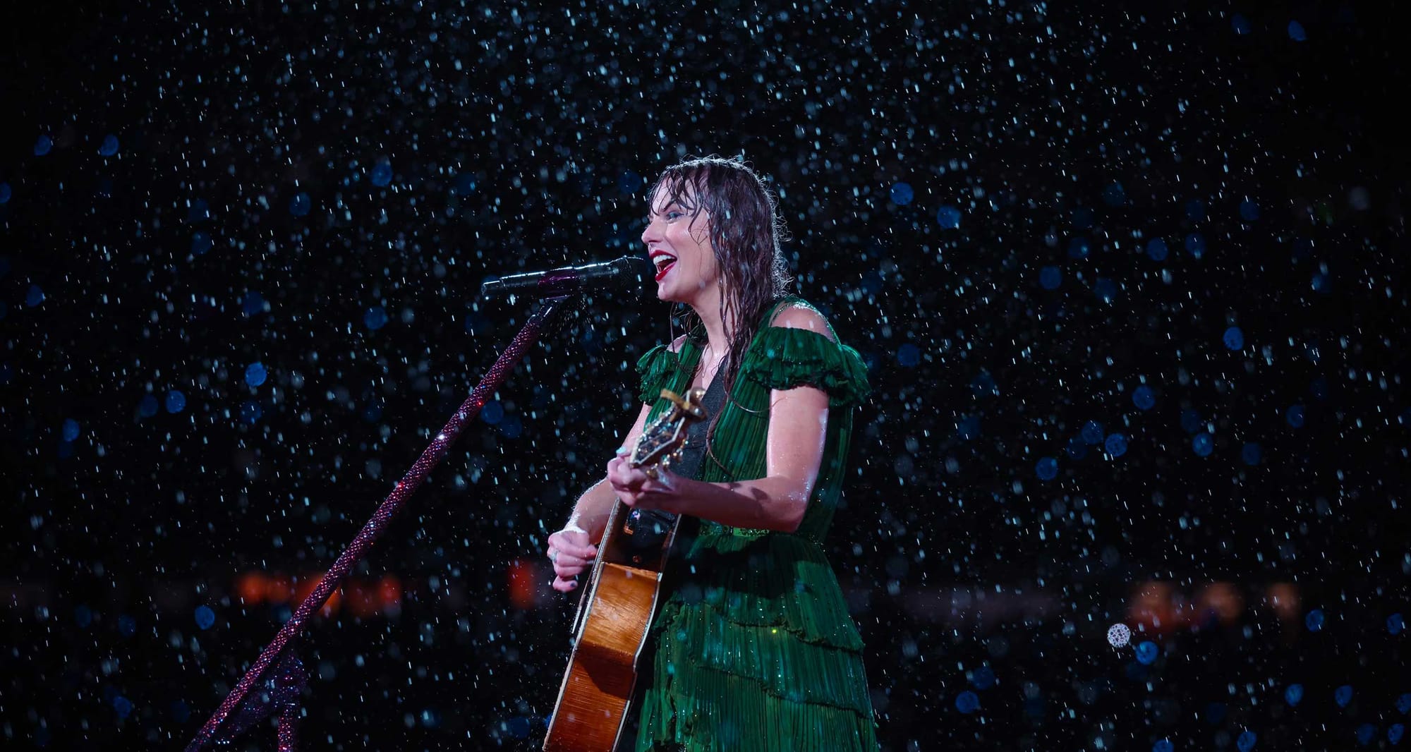 Taylor Swift singing in the rain while wearing a green dress and playing a guitar.