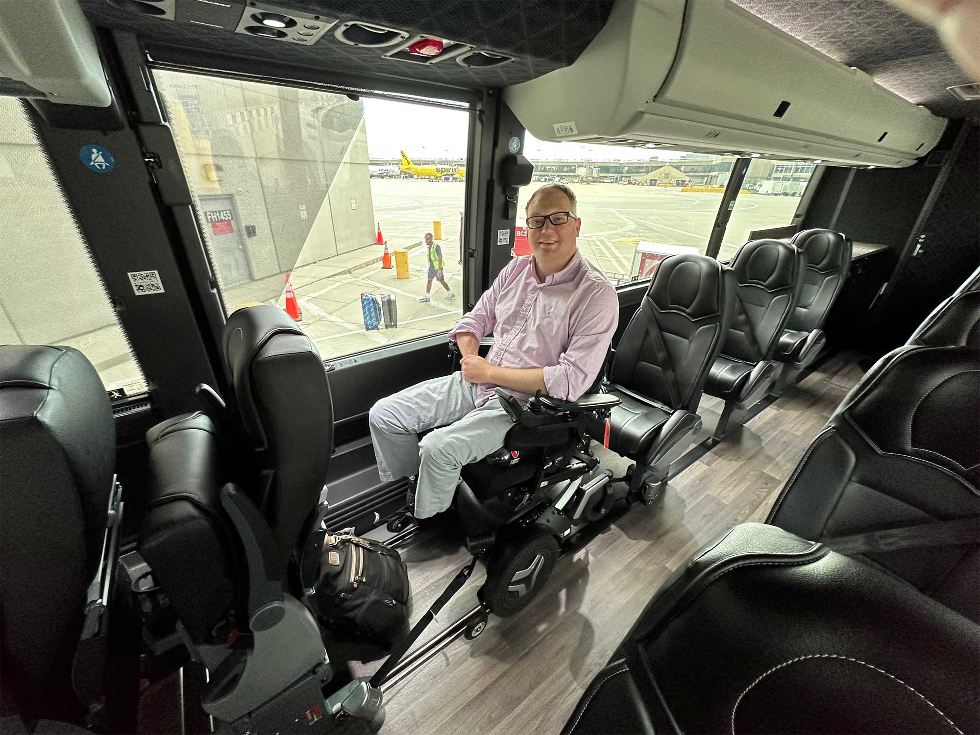 John seated in his wheelchair onboard a bus, the wheelchair is secured to the floor.