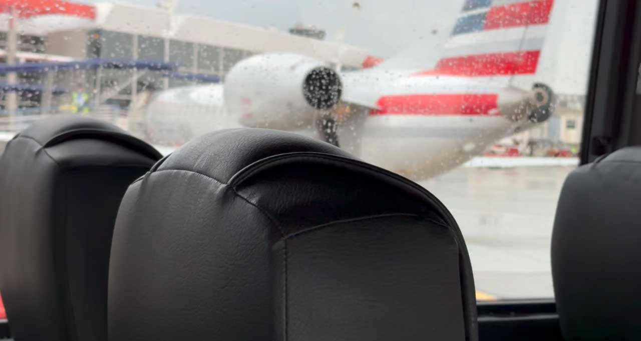 American Airlines airplane seen through rain-covered window of bus.