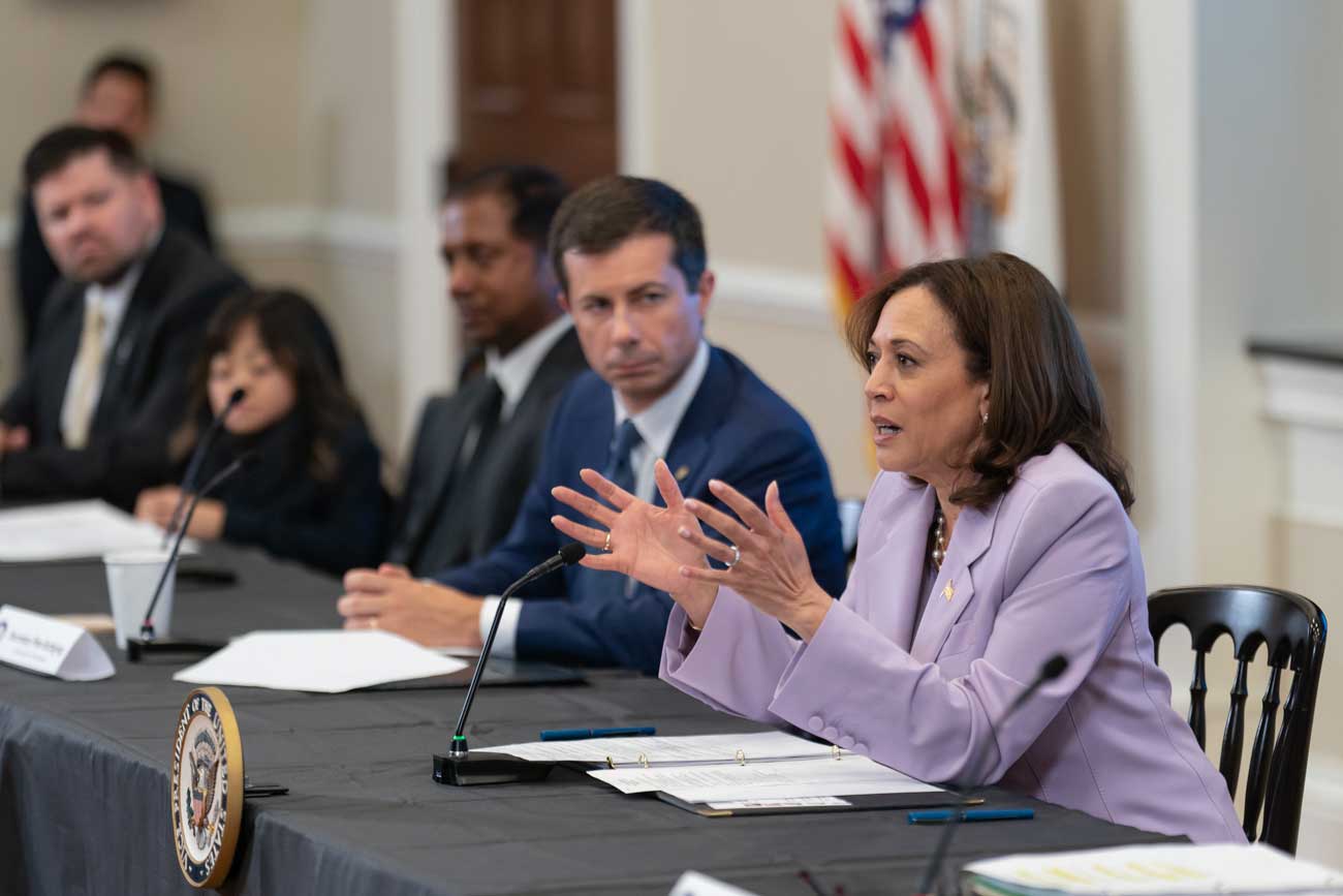 Kamala Harris speaking while seated at a table next to the Transportation Secretary.