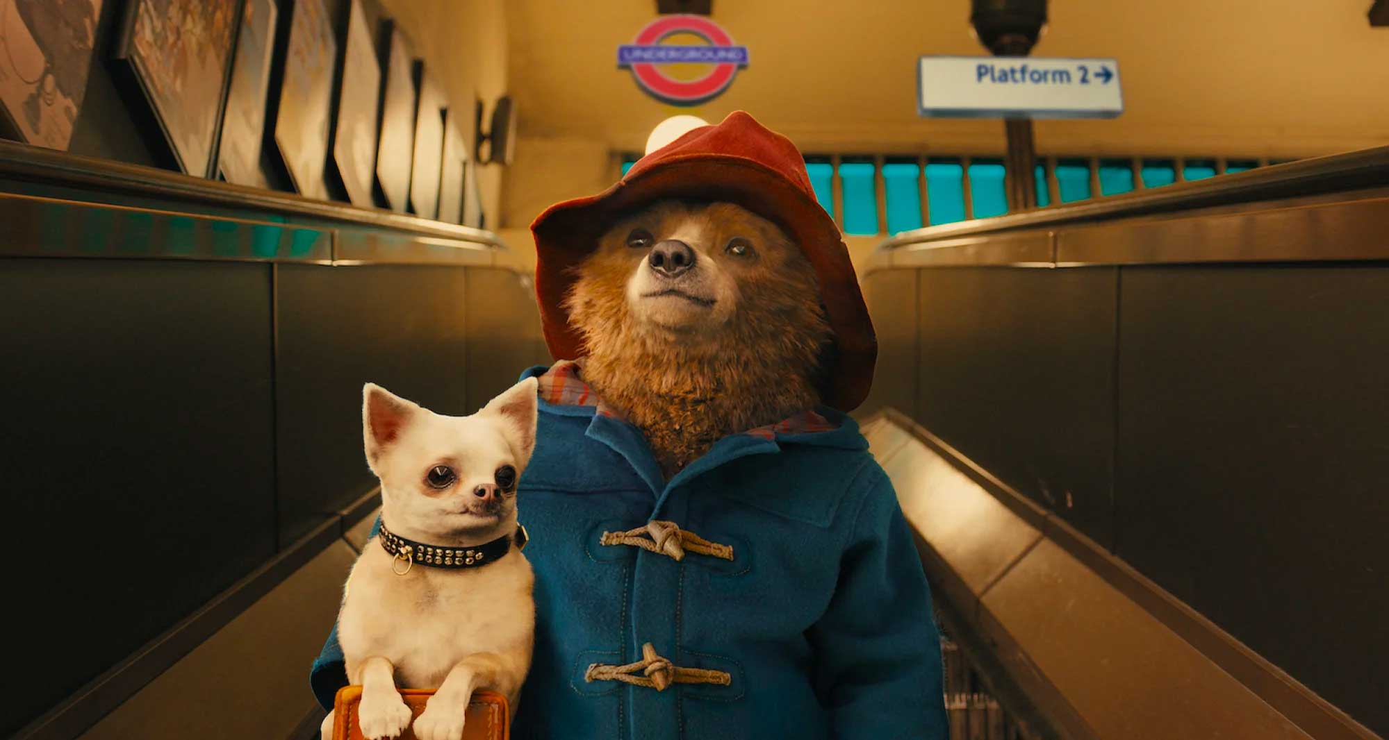 Paddington bear holding small dog while on escalator inside London tube station.