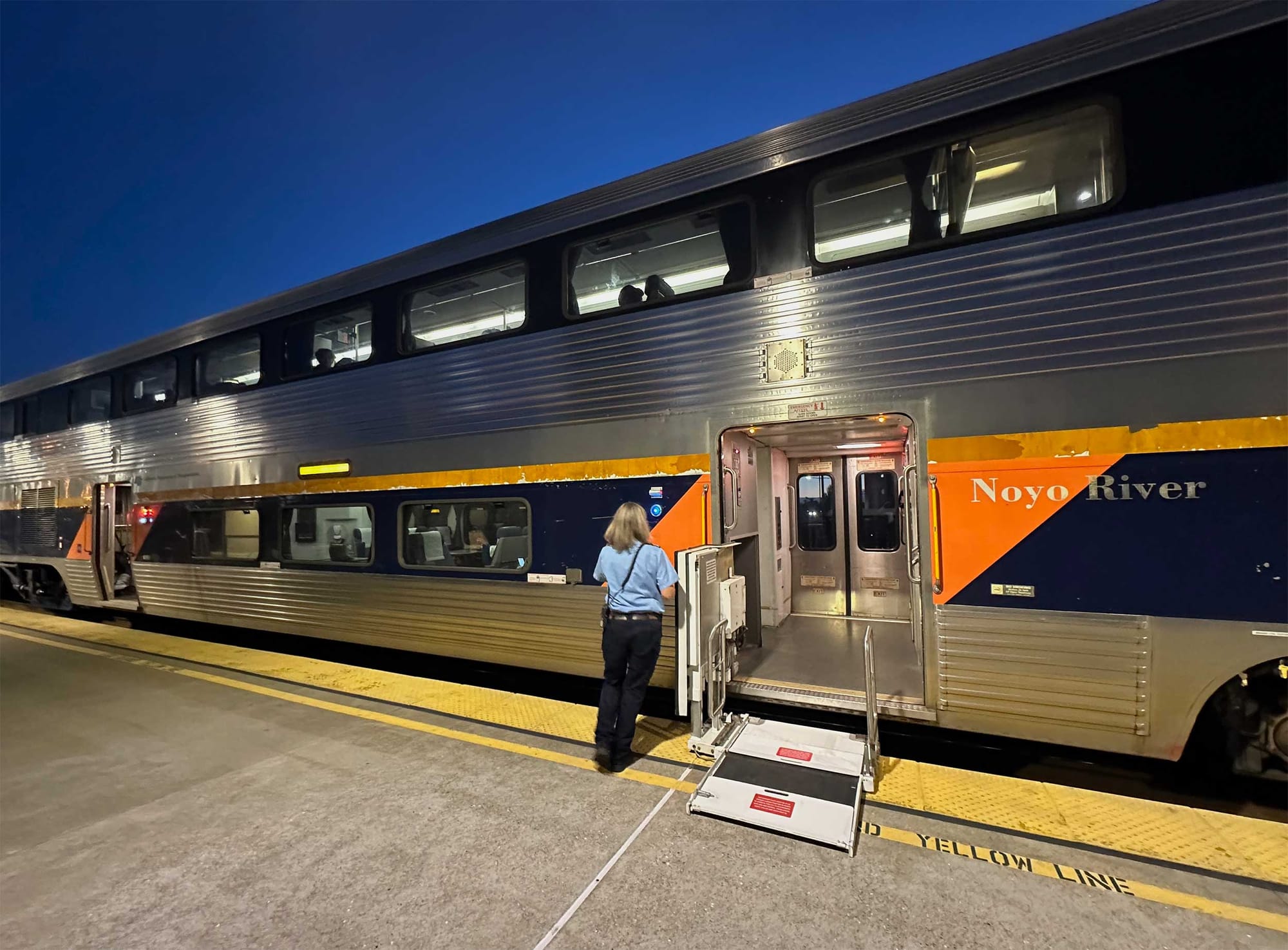 Train conductor deploying wheelchair lift onto station platform.