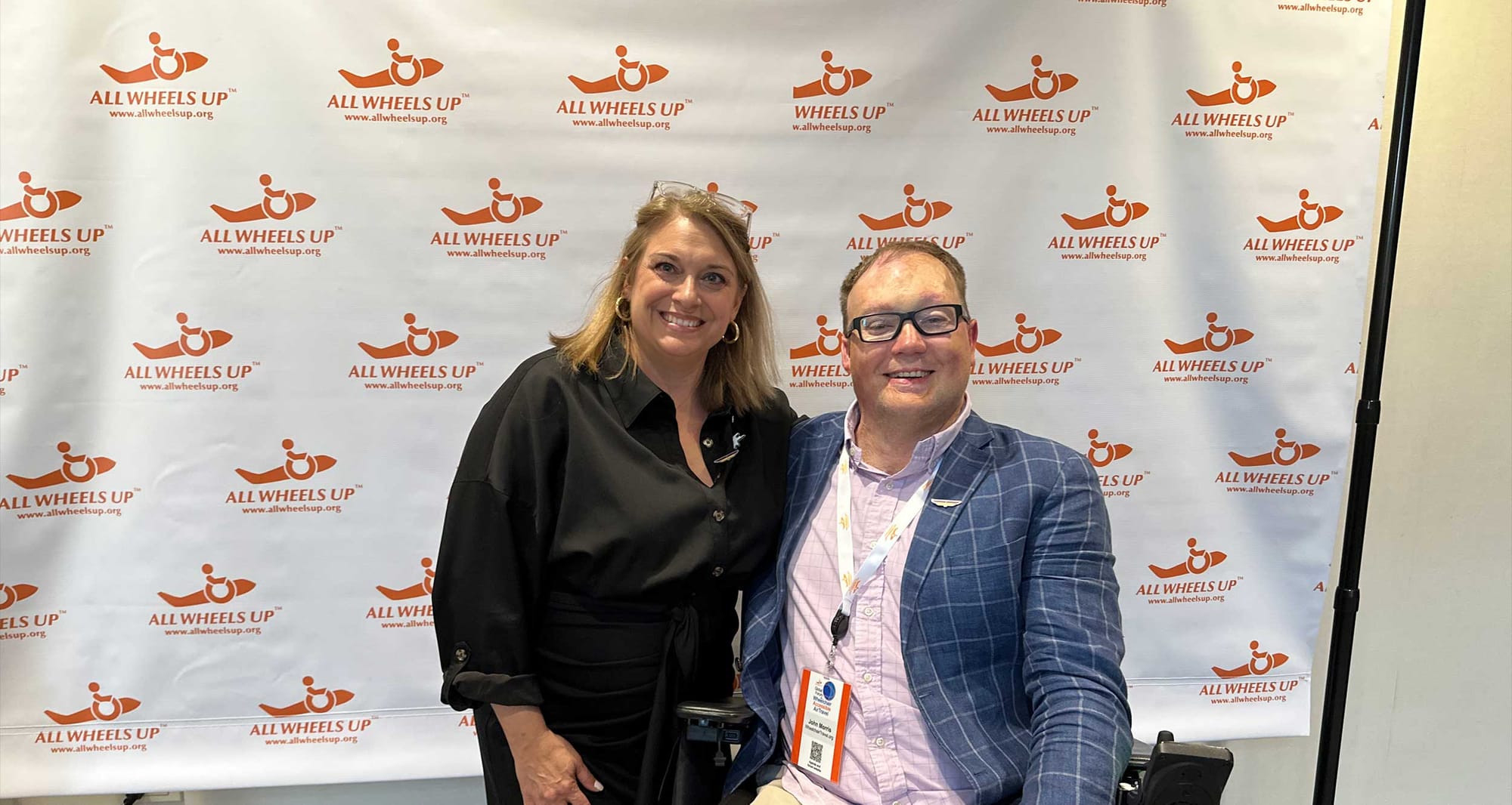 John with All Wheels Up founder Michele Erwin in front of logo banner.