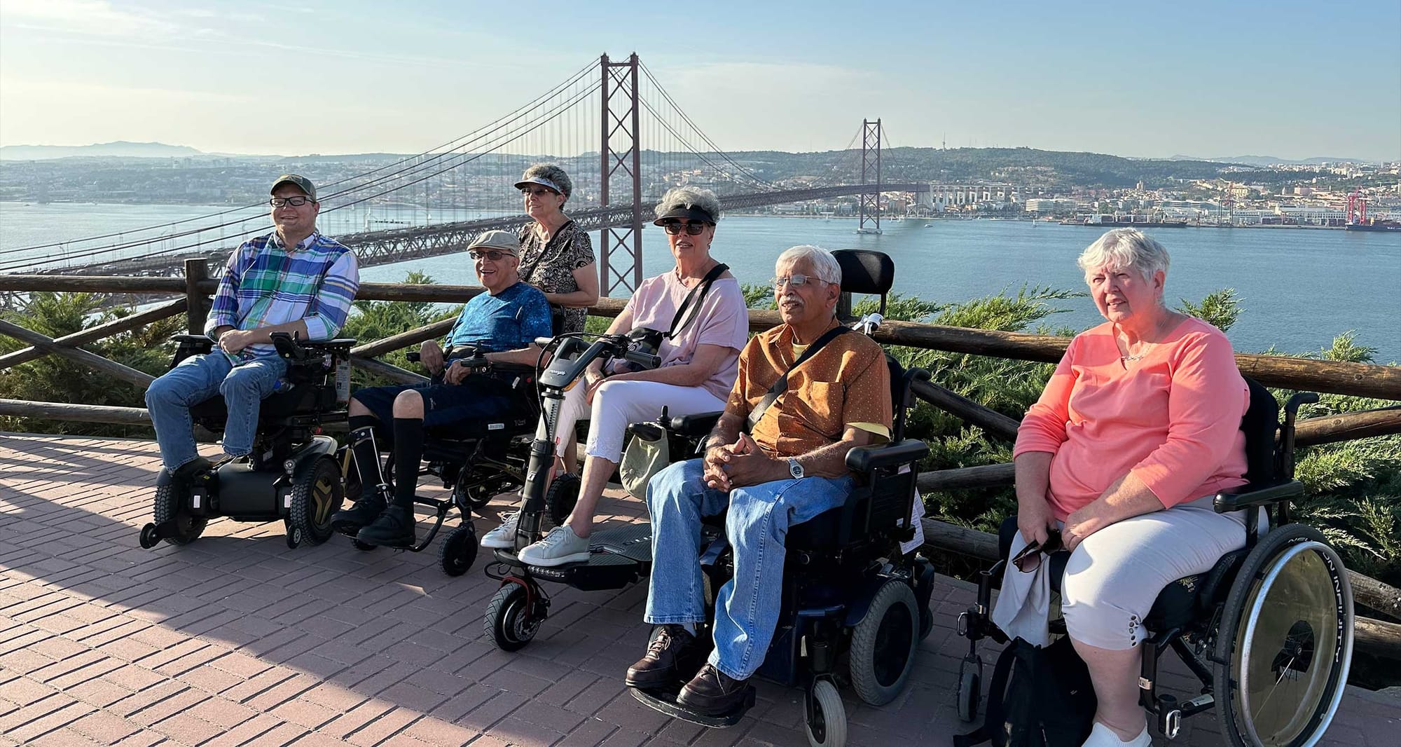 Group of wheelchair users in front of a bridge that crosses a river next to Lisbon city skyline.