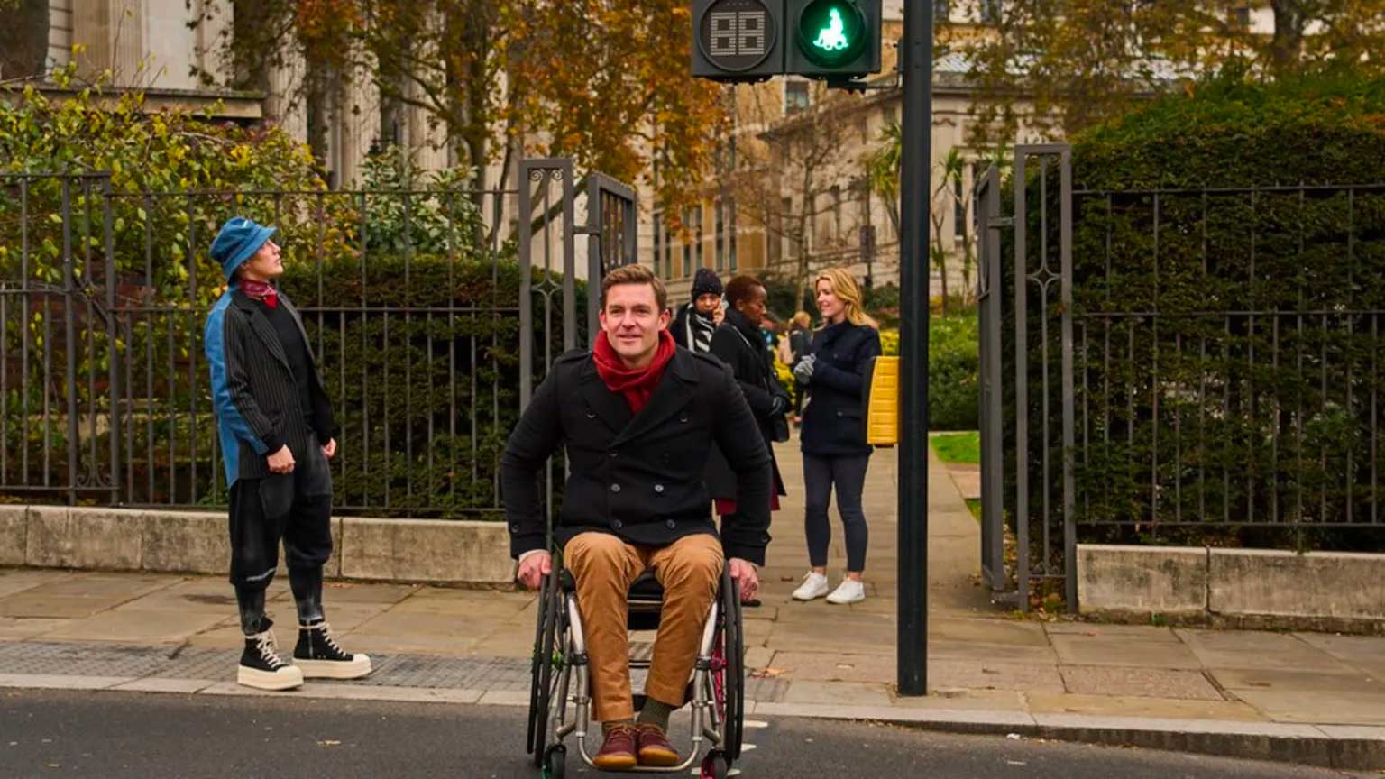 Male wheelchair user sitting beneath a crosswalk signal.