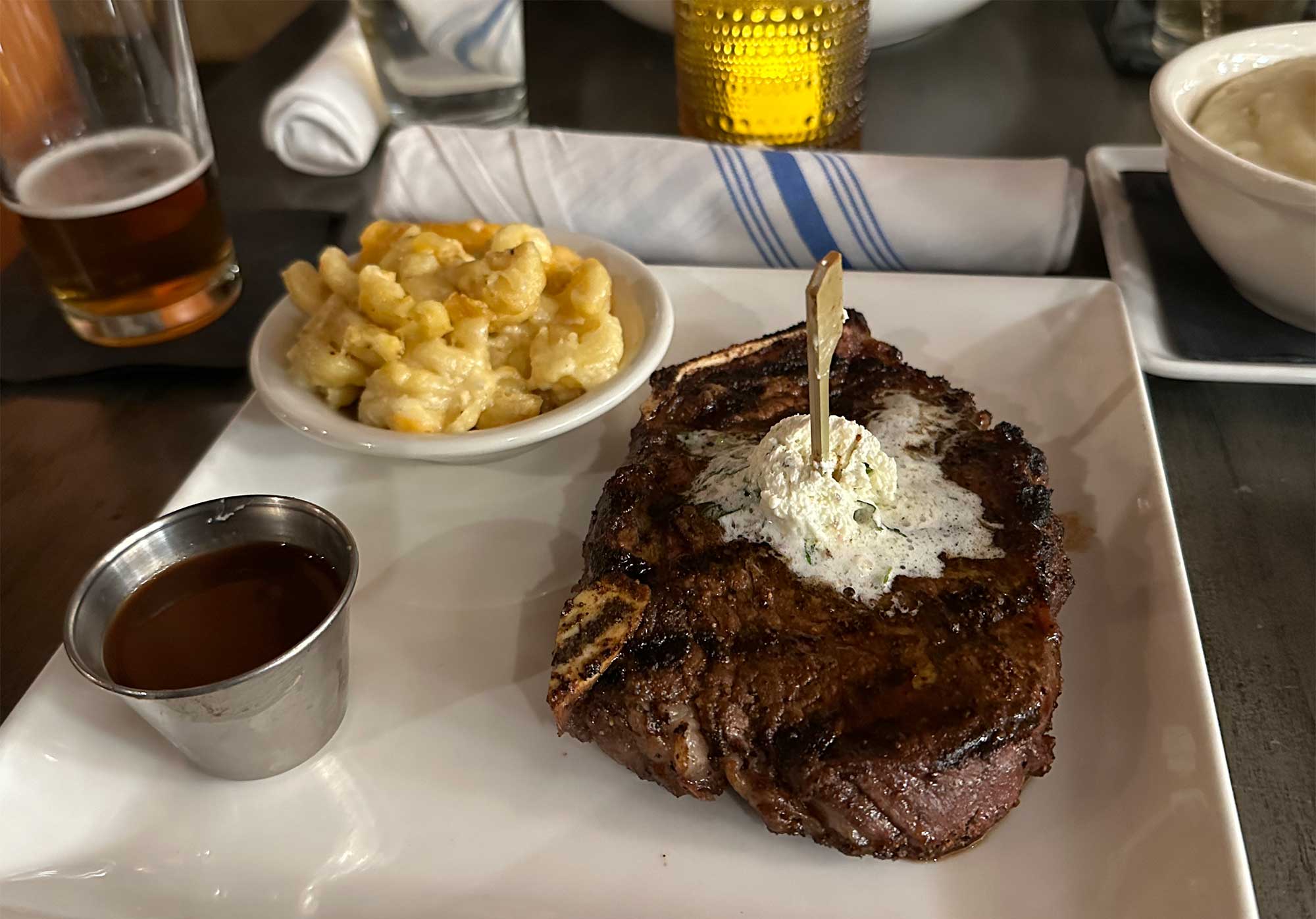 Bone in New York strip steak with macaroni and cheese and mashed potatoes.