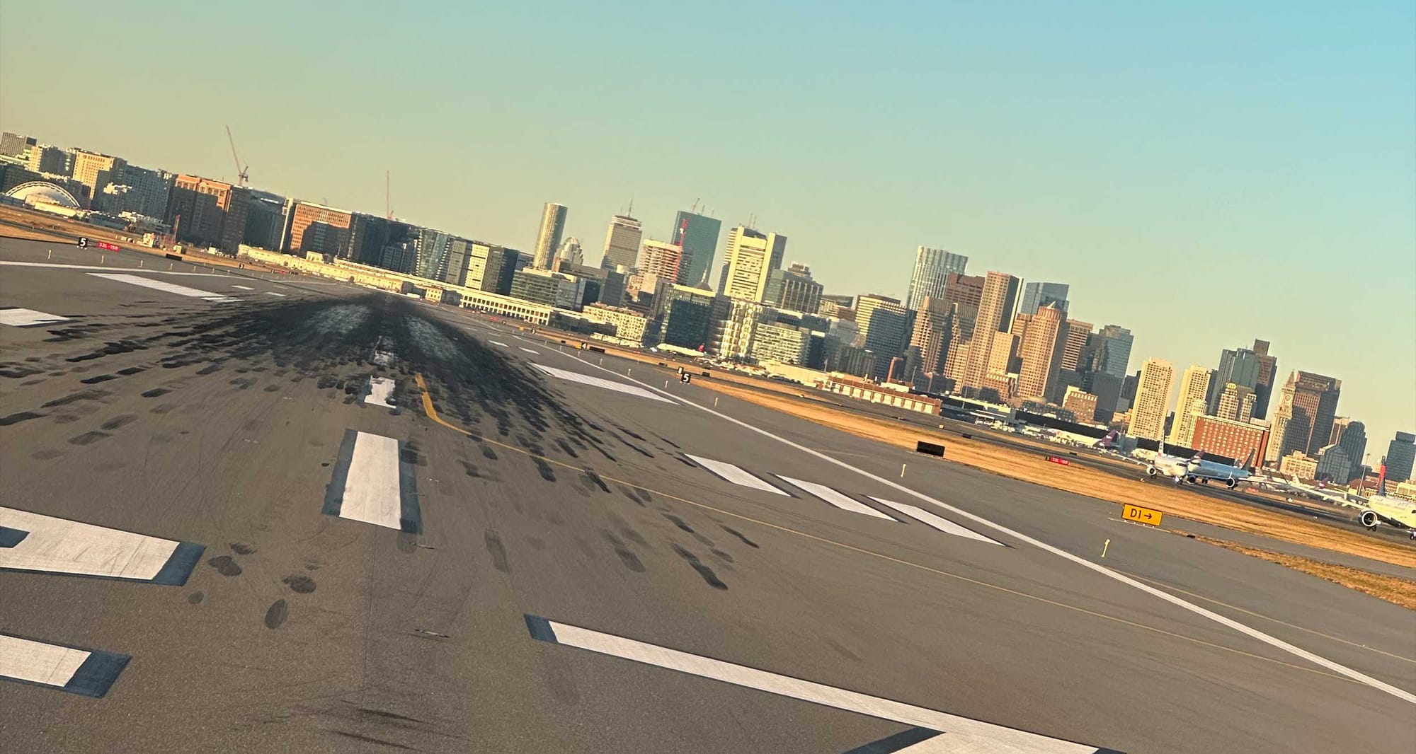 Boston city skyline seen in distance, beyond an airport runway.